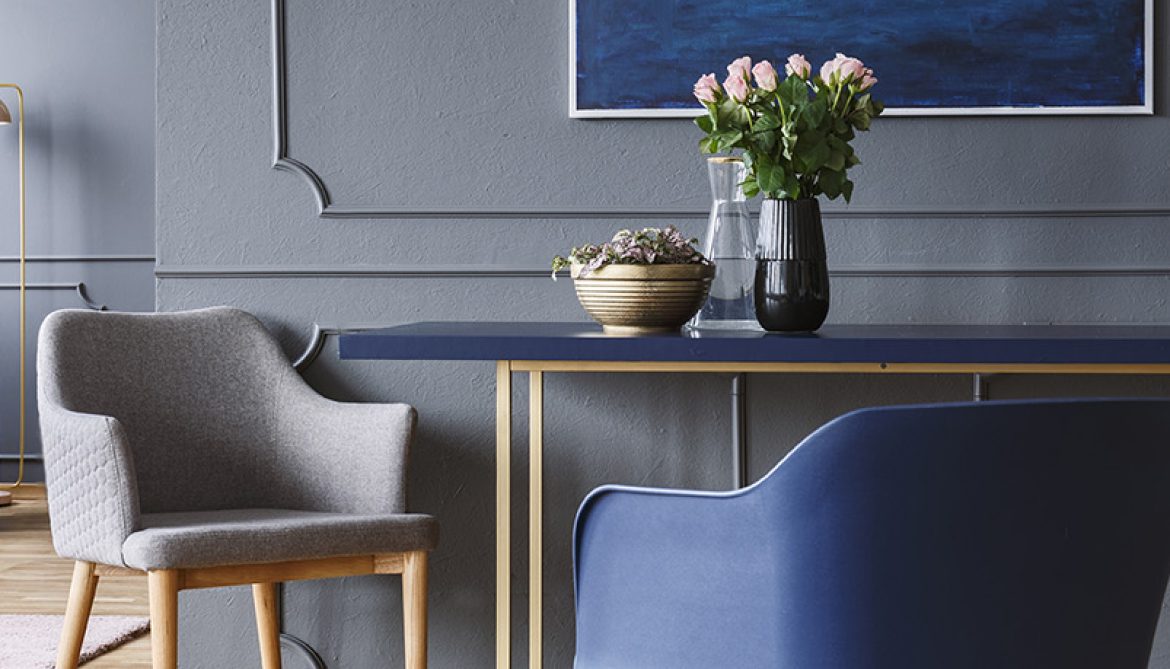 Chairs standing by the blue and gold dining table with pink roses in vase in dark grey open space living room interior